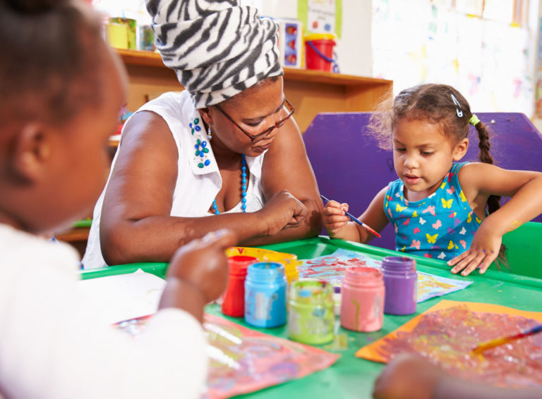 Teacher helping young student paint on sheet of paper