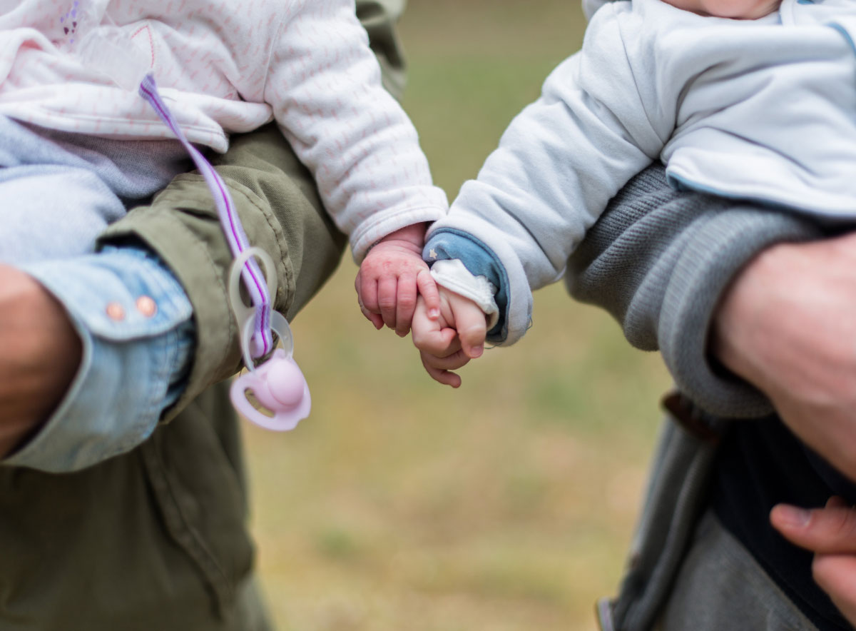 Two babies reaching out to hold hands while being held by parents