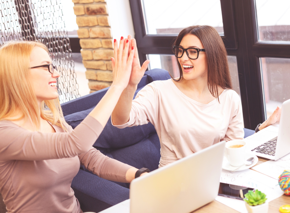 Two women give high five while collaborating on a laptop