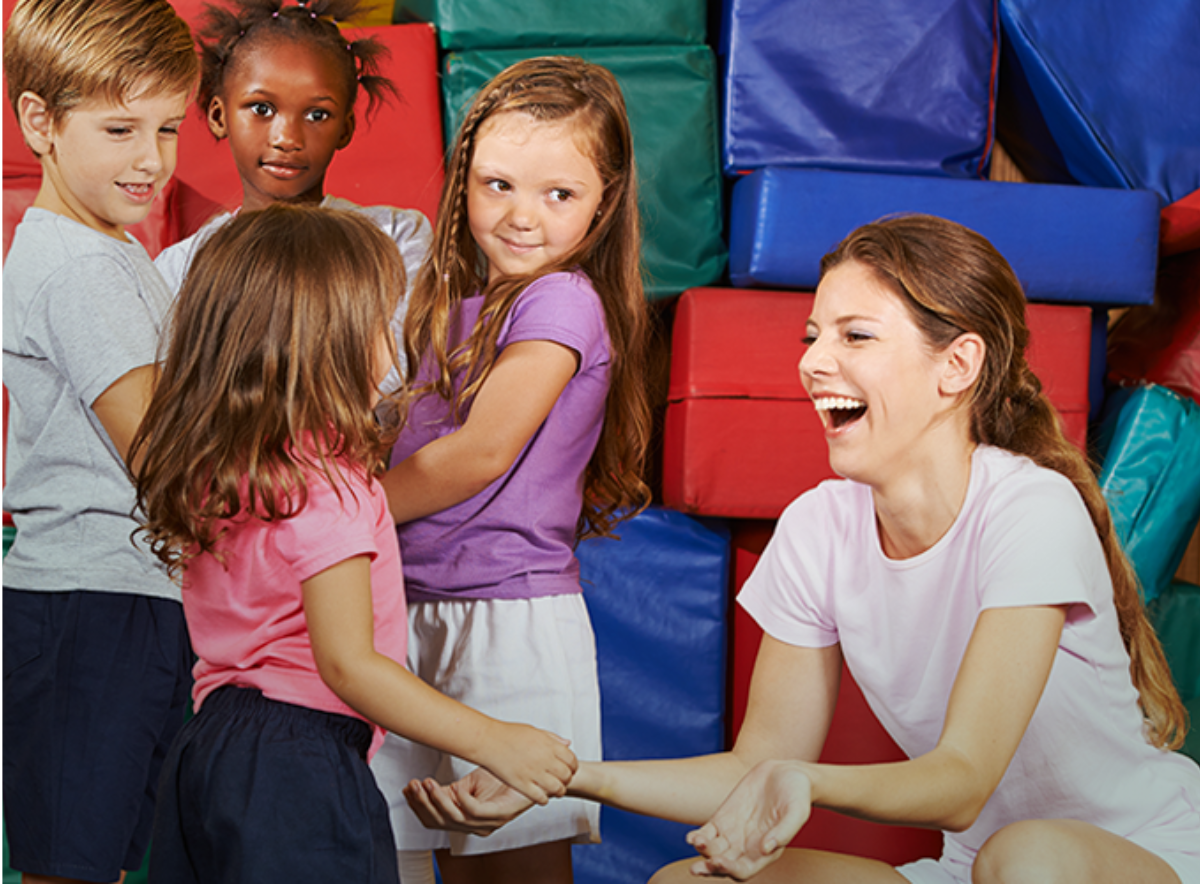 Children in gym with watching girl and teacher reach for each other and laughing