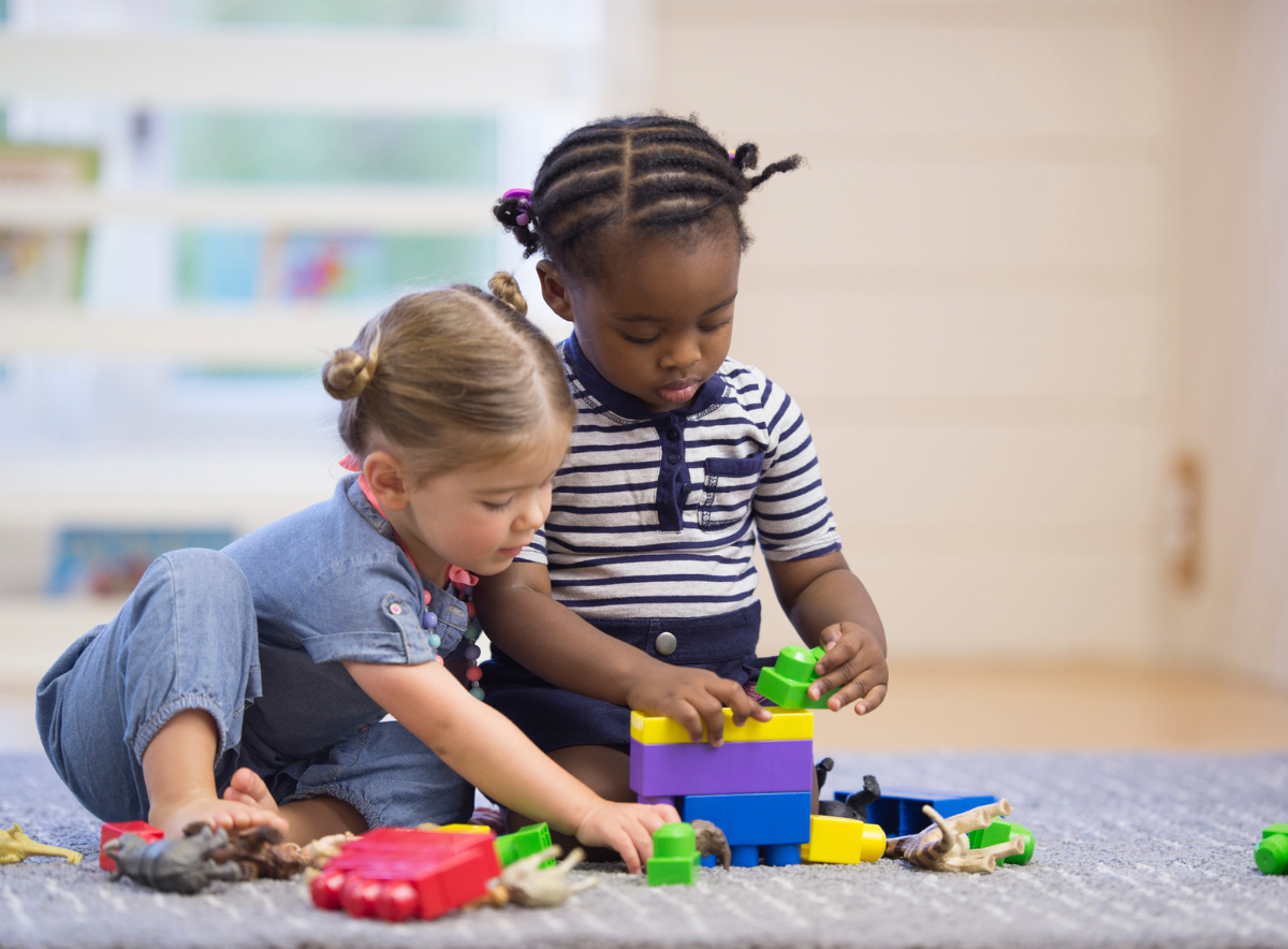 Young girls sit on the floor and share toys while playing at a child care center