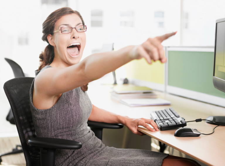 Business woman at a desk lauging and pointing in an unfriendly teasing manner