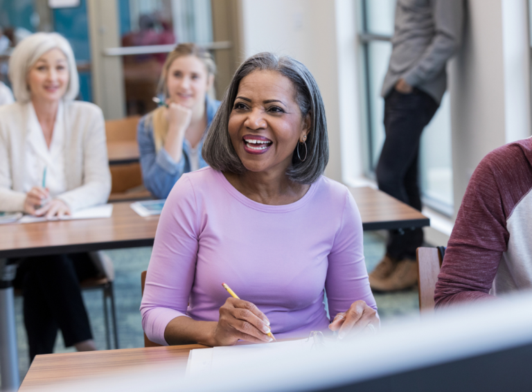 Woman sitting at a desk smiles during a preschool meeting with staff and parents