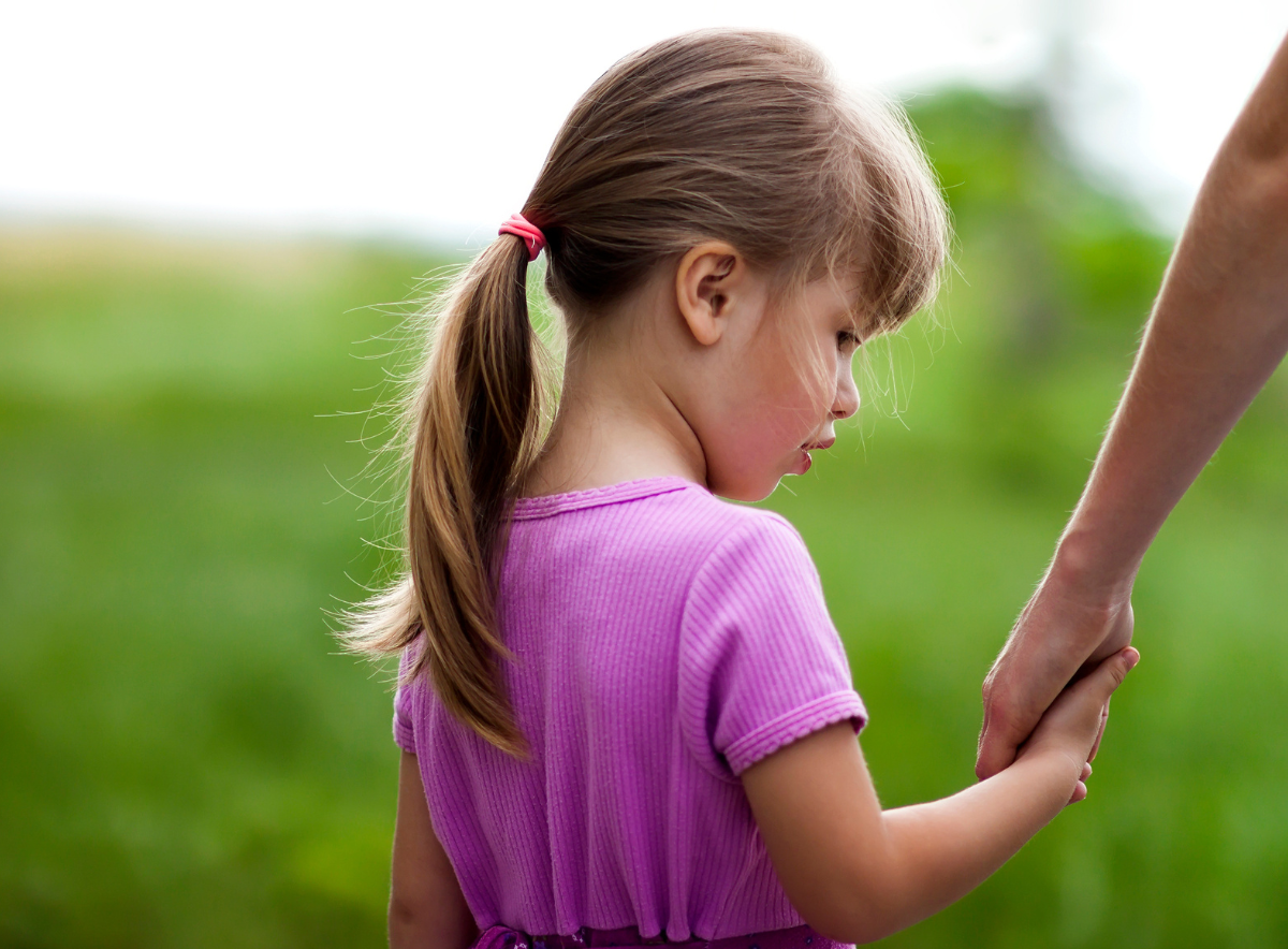 Young girl looks sad while holding an adult's hand