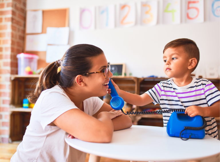 Boy holding pretend phone to child care teacher to learn phone etiquette