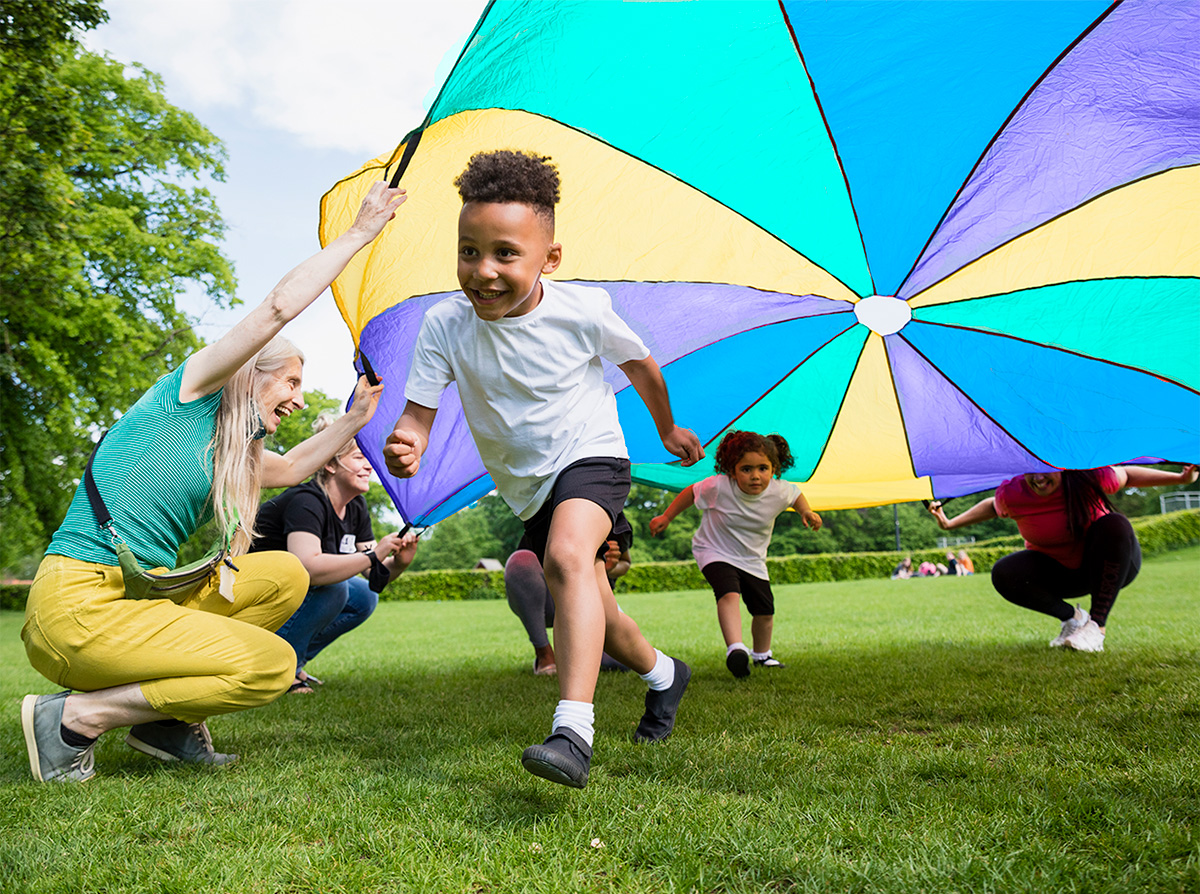 Parents playing with young kids with parachute game at child care center event