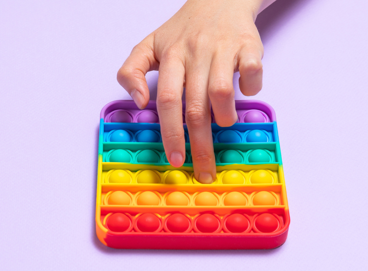 Child's hand with a push pop bubble toy in rainbow colors