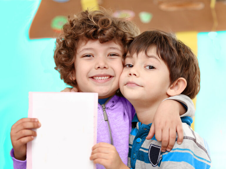 Two boys hug and smile as one holds up paper.