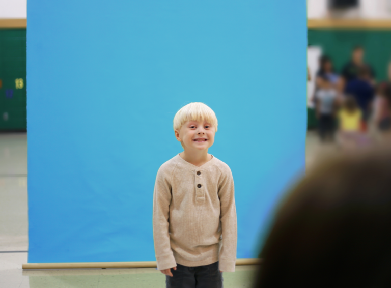 Smiling boy stands in front of blue screen for school photo