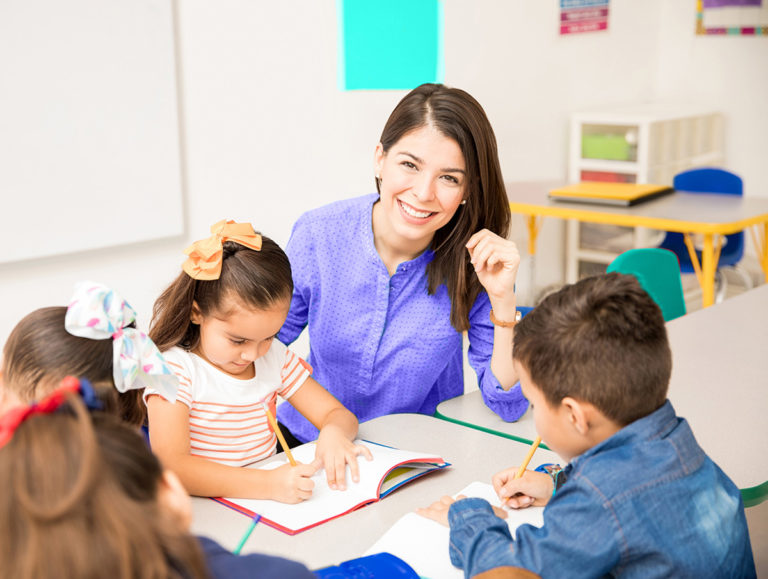 smiling-teacher-children-writing-table