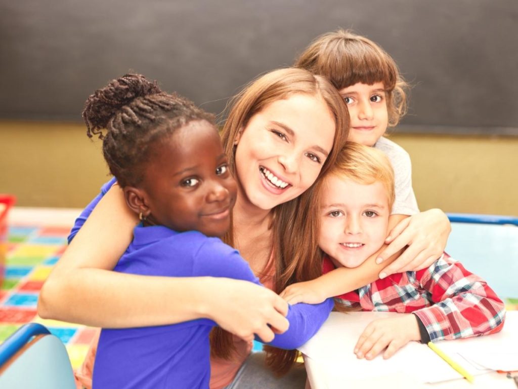 Kids surround a young woman teacher with hugs