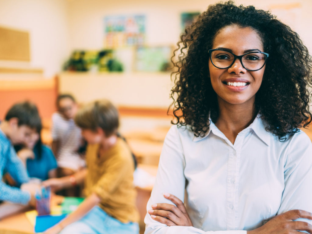 A teacher smiles as her students work behind her.