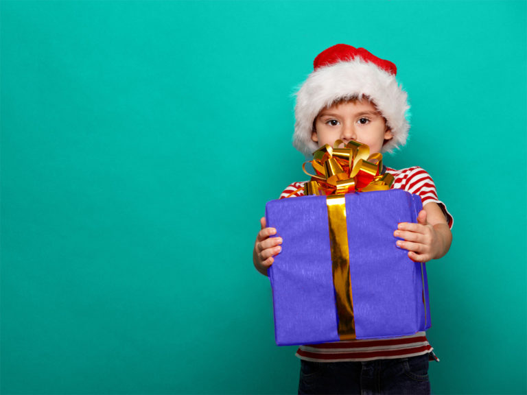 Young boy wearing Santa hat holding large purple wrapped gift