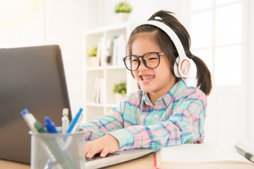 A young girl wears headphones and sits in front of a laptop.
