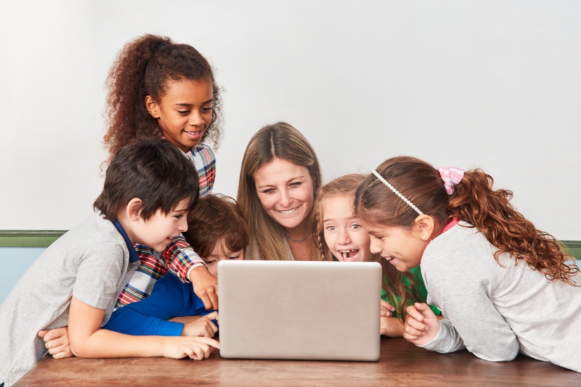 Children gather around a teacher and her laptop computer.