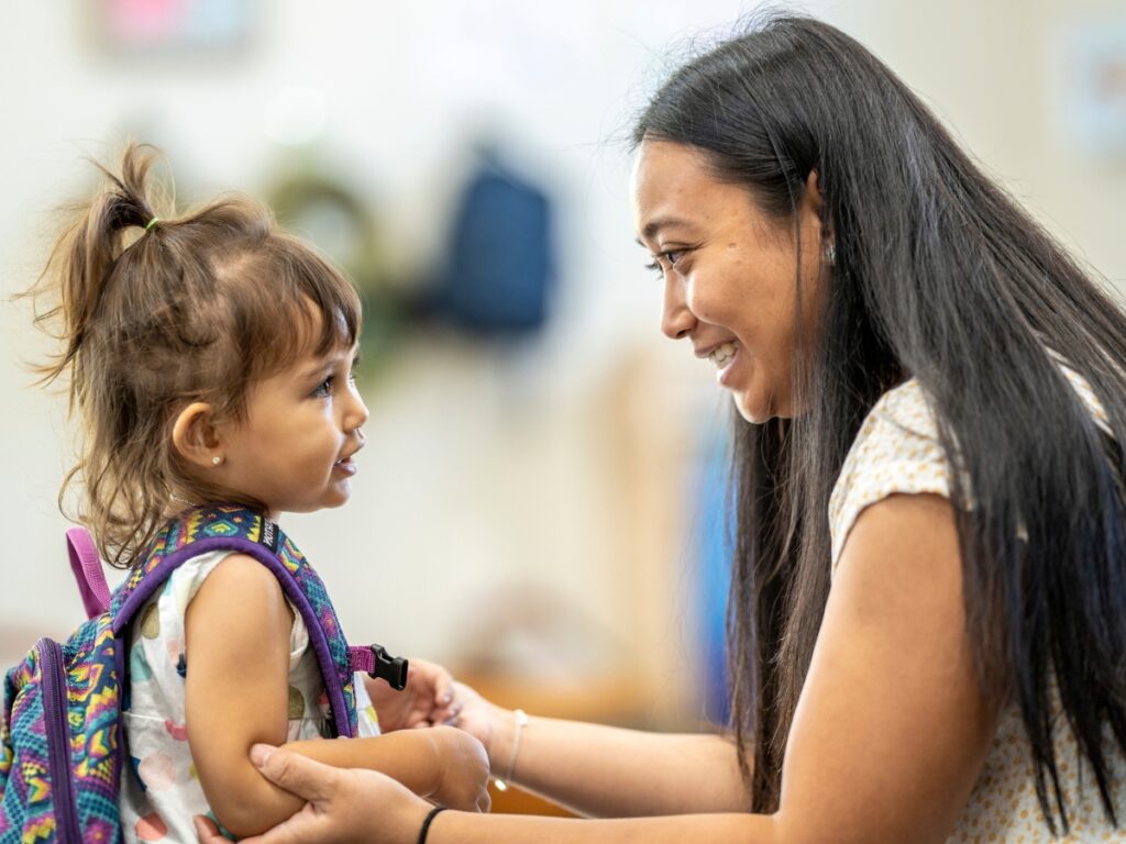 A teacher welcomes a young student into her classroom.