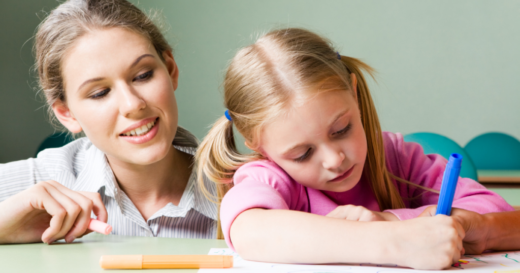 A teacher watches on as a student writes with a marker.