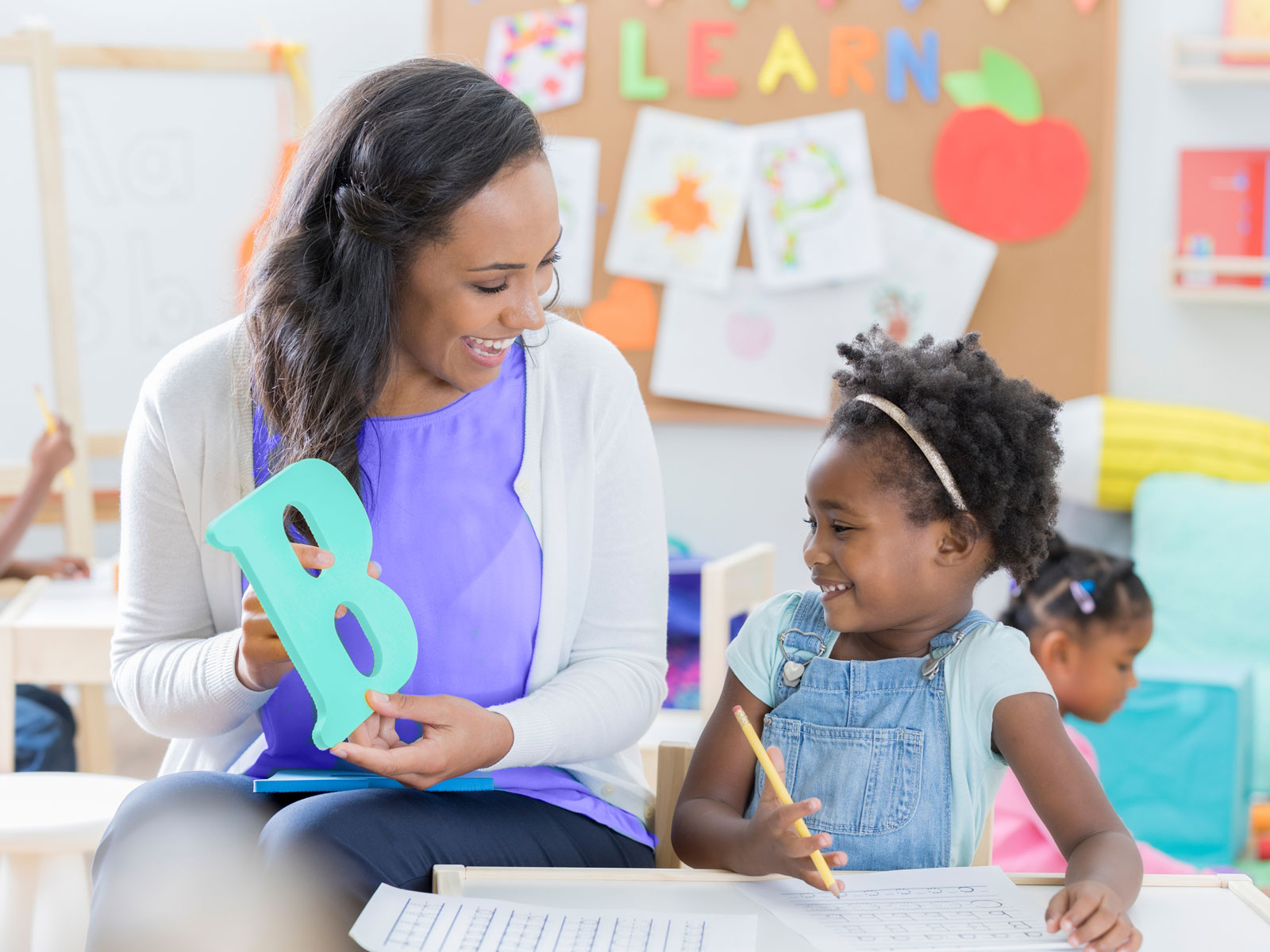 Daycare teacher holding letter B for young girl