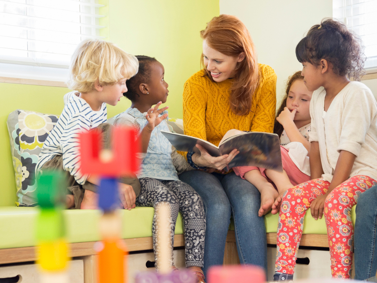 A teacher reads a story to four students nearby.