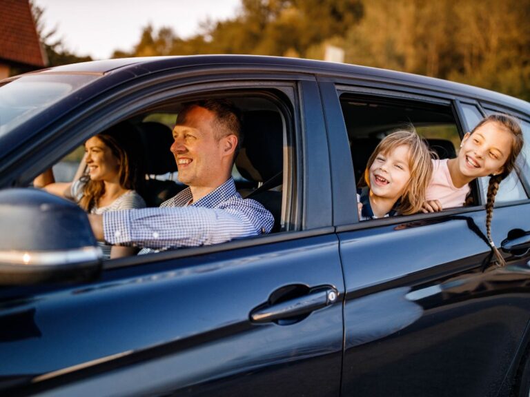 A family in a black car happily ride together on a road trip.