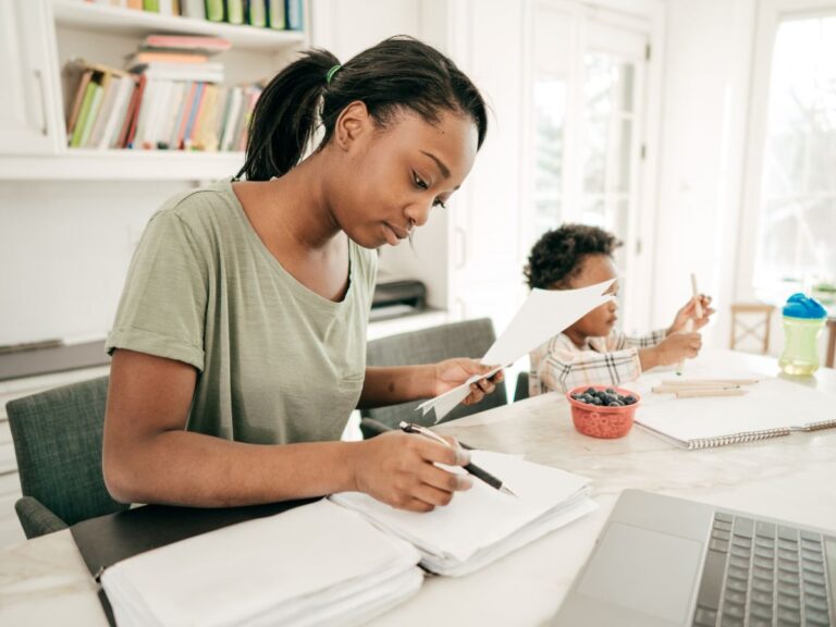 Mother files taxes while her child draws nearby.