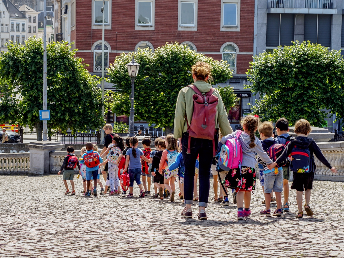 A Teacher guides her students while walking in the city.